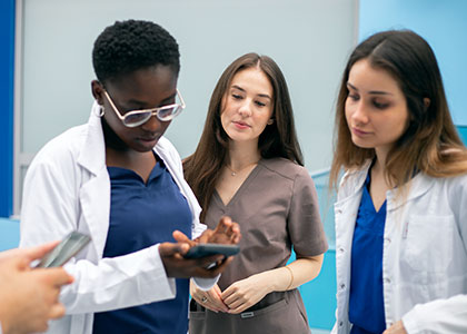 3 nursing students looking down at a phone held by one of the nurses